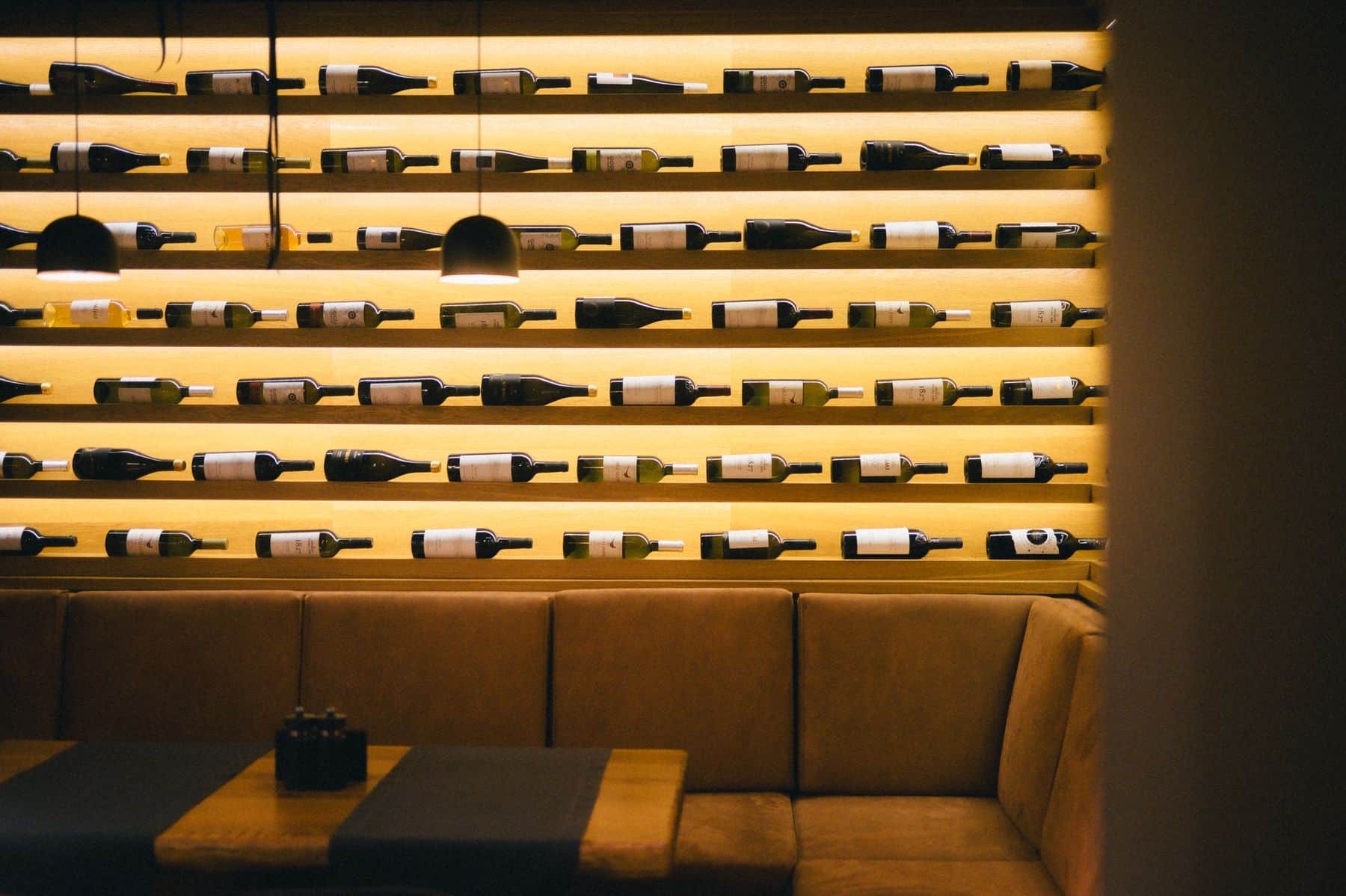 A bar counter with shelves of bottles lit warmly in the evening