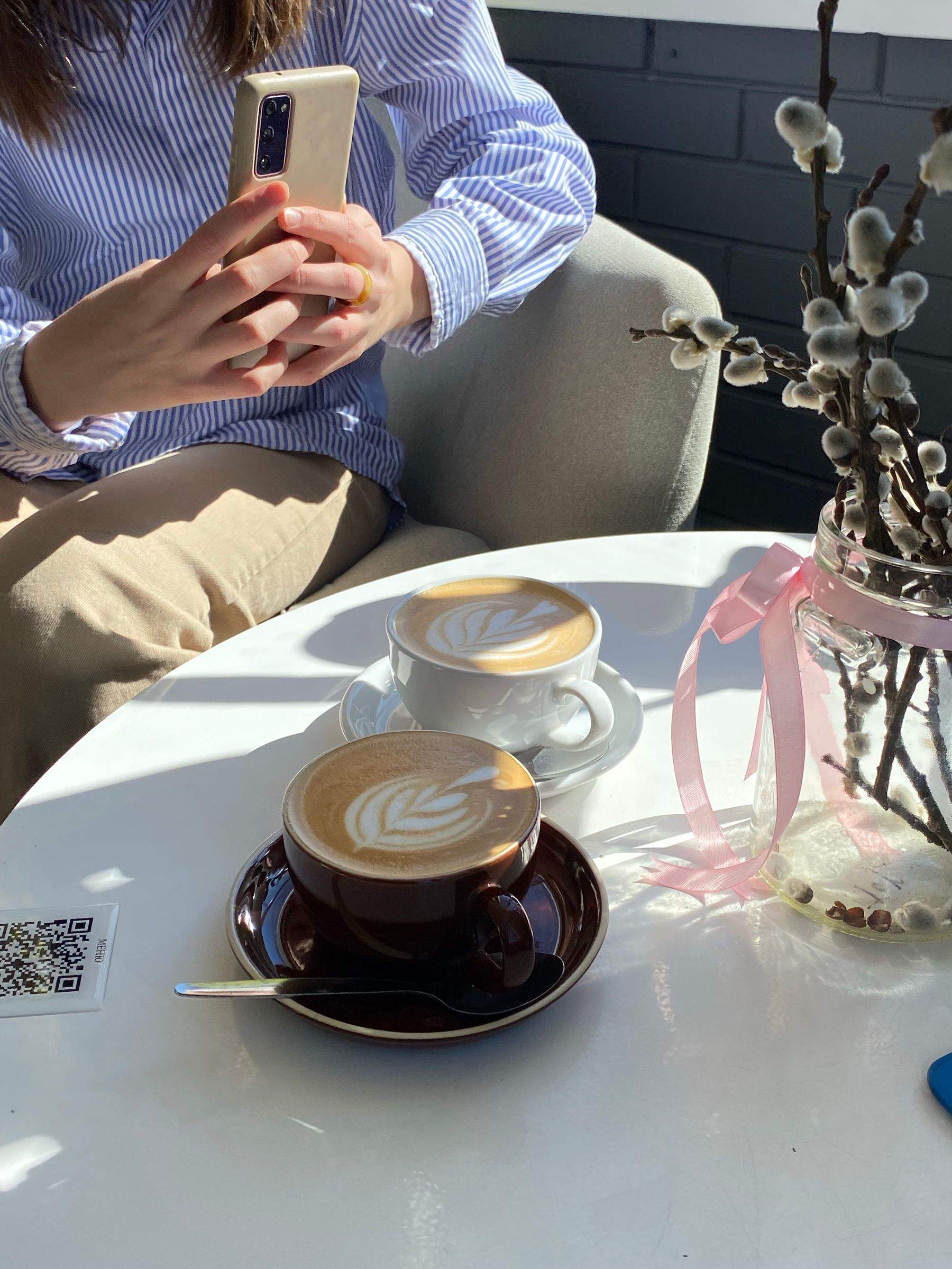 A guest holding a phone at a café table with two coffees and a QR code